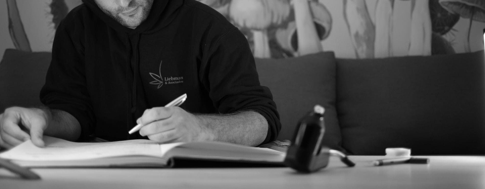 Persona firmando documentos en un escritorio, con un buzo de Liebman & Asociados